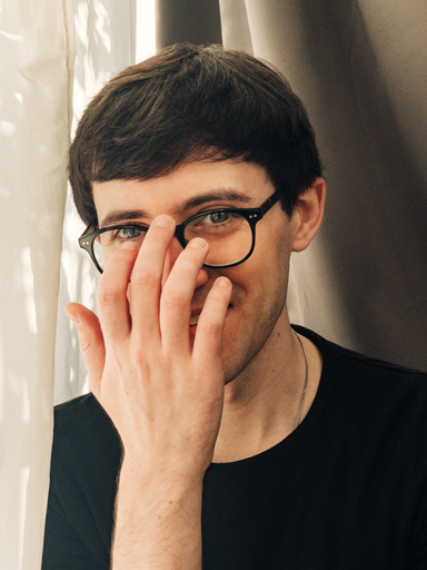 Retrato do Matthew sorrindo para a câmera enquanto ajeita os óculos.