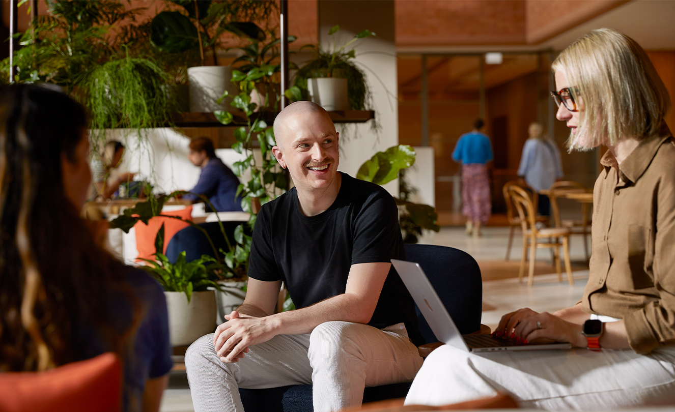 Trois personnes de l’équipe Apple, dont une avec un MacBook, discutant ensemble assises dans des fauteuils au Caffè Macs.