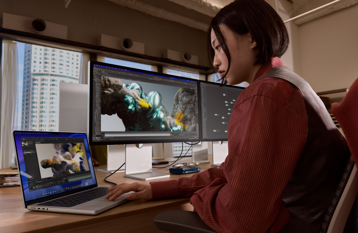 Eine Person in einem Büro arbeitet an einem MacBook Laptop, der über einen Thunderbolt 5 Anschluss mit einem Studio Display XDR verbunden ist