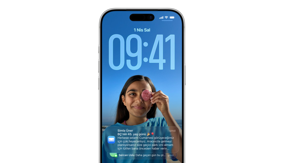 iPhone Kilit Ekranı’nda bir fotoğraf, Liquid Glass efektiyle saat rakamları, ekranın altında iki bildirim görünüyor