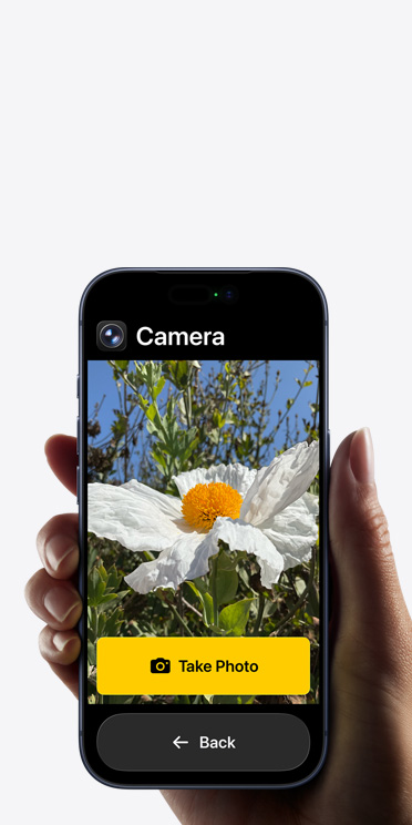 Layar iPhone 17 Pro menampilkan antarmuka aplikasi Kamera yang disederhanakan dengan bunga putih di dalam frame, tombol “Ambil Foto”, dan tombol "Kembali" di bawah