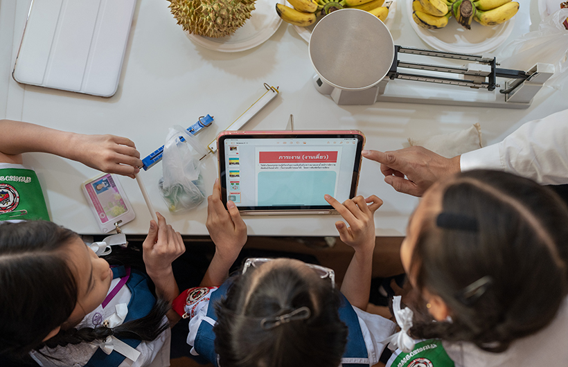 Tres estudiantes de enseñanza básica alrededor de un iPad colaborando en una presentación de un proyecto de ciencias.