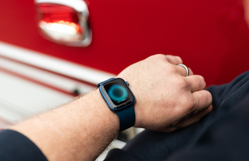 Une Apple Watch portée au poignet affiche le message : Maintenant, inspirez, avec un camion de pompiers à proximité