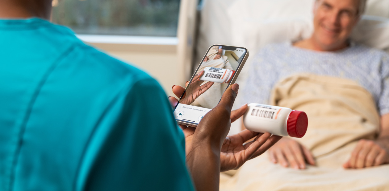 Een verpleegster in blauwgroene kleding scant de medicijnen van een patiënt met haar iPhone.