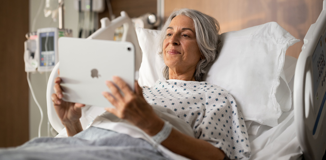 Een vrouwelijke patiënt ligt in een ziekenhuisbed en kijkt naar haar iPad.