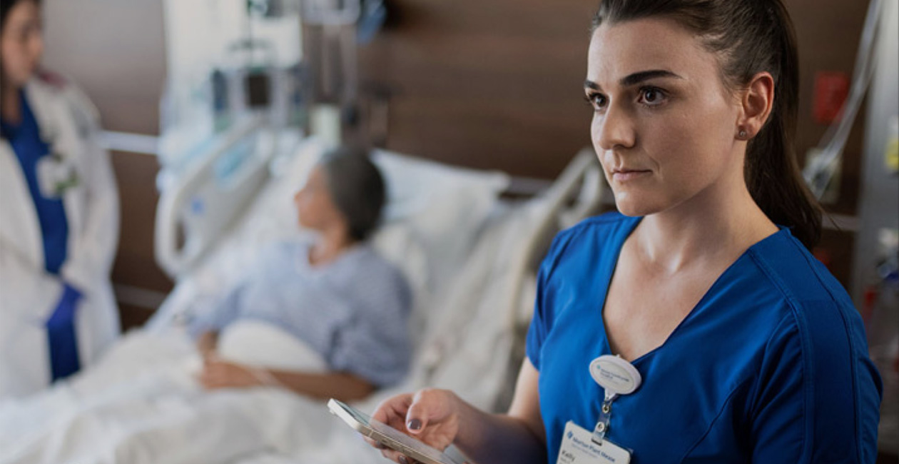 En sygeplejerske skriver på sin iPhone, mens en læge taler med en patient.